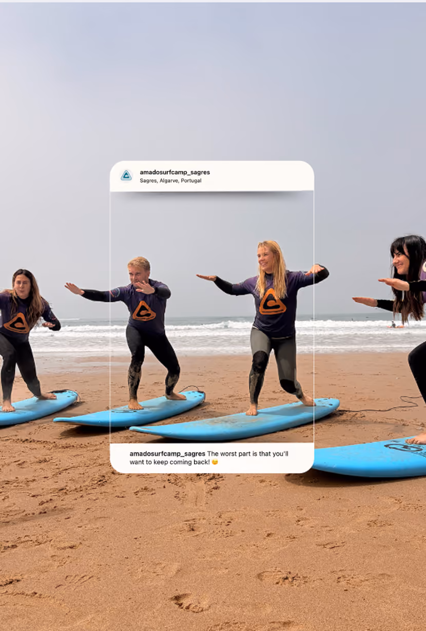 Four people in wetsuits practicing surfing stances on blue boards on a sandy beach with ocean waves.