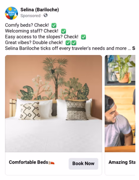 White bed with two patterned pillows against a peach wall with green plants behind the headboard.