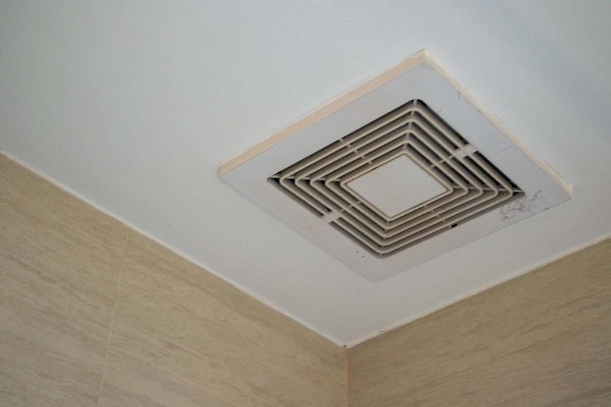Ceiling-mounted bathroom exhaust fan with a white vent cover, surrounded by beige tiles. T