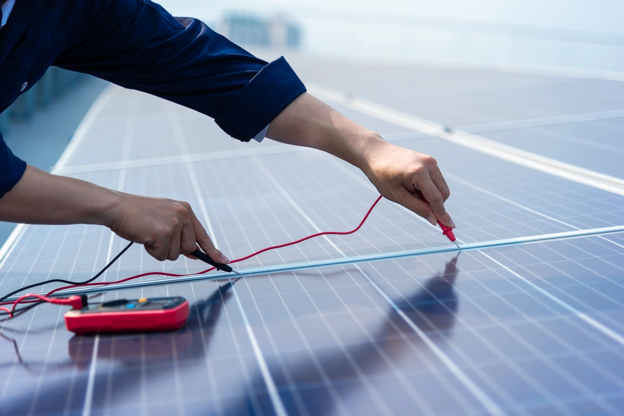 Hands holding a multimeter with red and black probes, testing solar panels.
