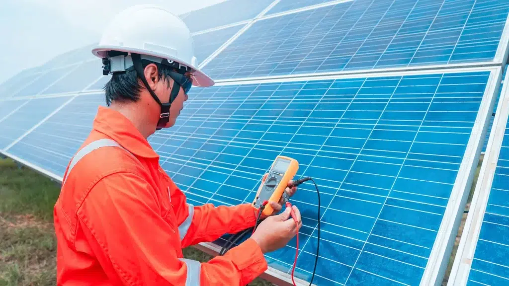 Technician in safety gear inspecting solar panels with multimeter, emphasizing solar panel inspection services for optimal performance and safety in Chula Vista.