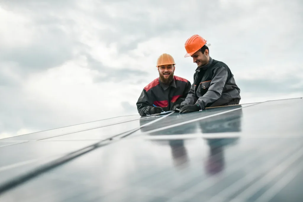 Two technicians installing solar panels on a rooftop, smiling and collaborating, with cloudy sky in the background, emphasizing solar energy solutions in San Diego.
