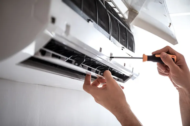 Hands using a screwdriver to service a ductless mini-split air conditioning unit, illustrating HVAC maintenance expertise relevant to West Coast Heating, Air Conditioning, and Solar's services in Ramona, CA.