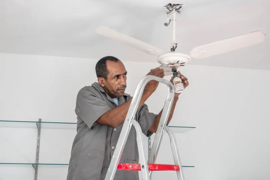 Technician installing a whole house fan on a ladder, demonstrating energy-efficient cooling solutions for homes in San Diego.