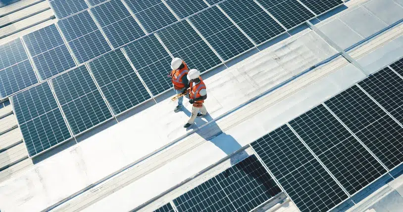 Two technicians in safety gear walking on a roof covered with solar panels, representing the installation of photovoltaic systems for renewable energy in San Diego.