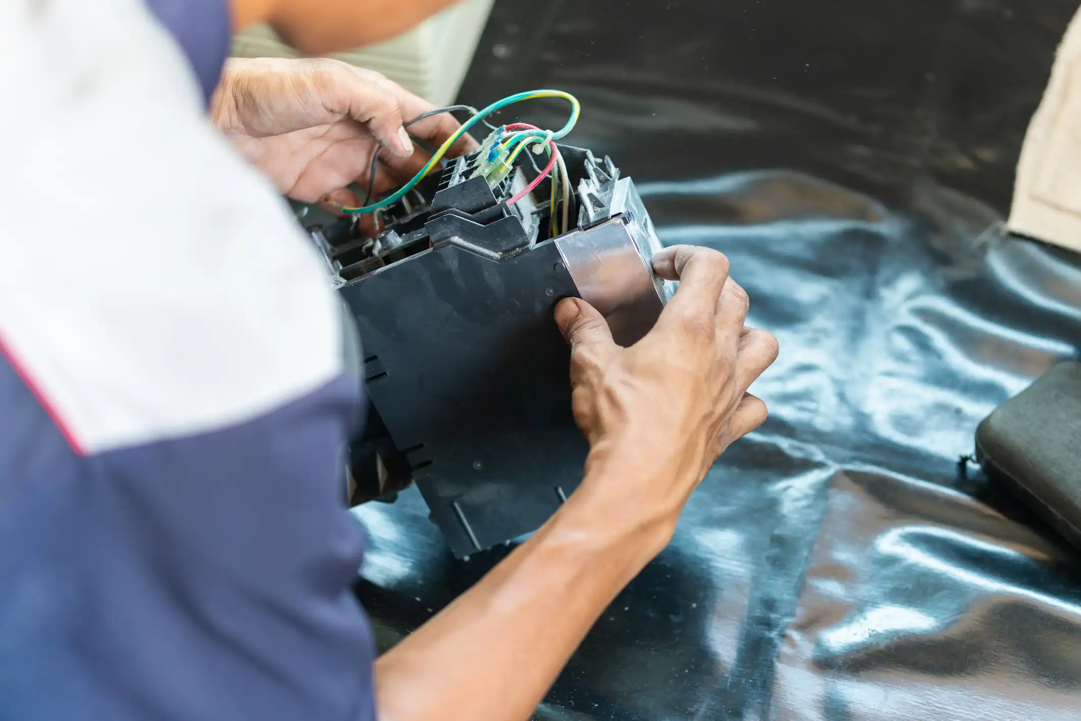 Close-up of hands working on a black electronic or mechanical device with exposed wires.
