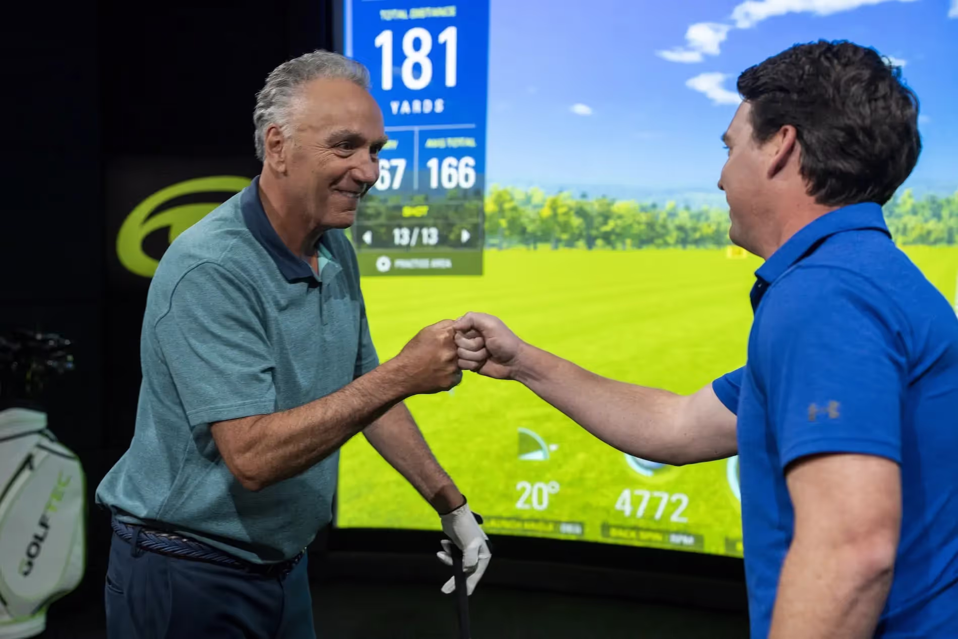 Student and coach fist bumping in a GOLFTEC center practice bay