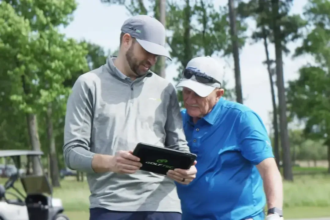 Coach and student viewing iPad on golf course to break down shots