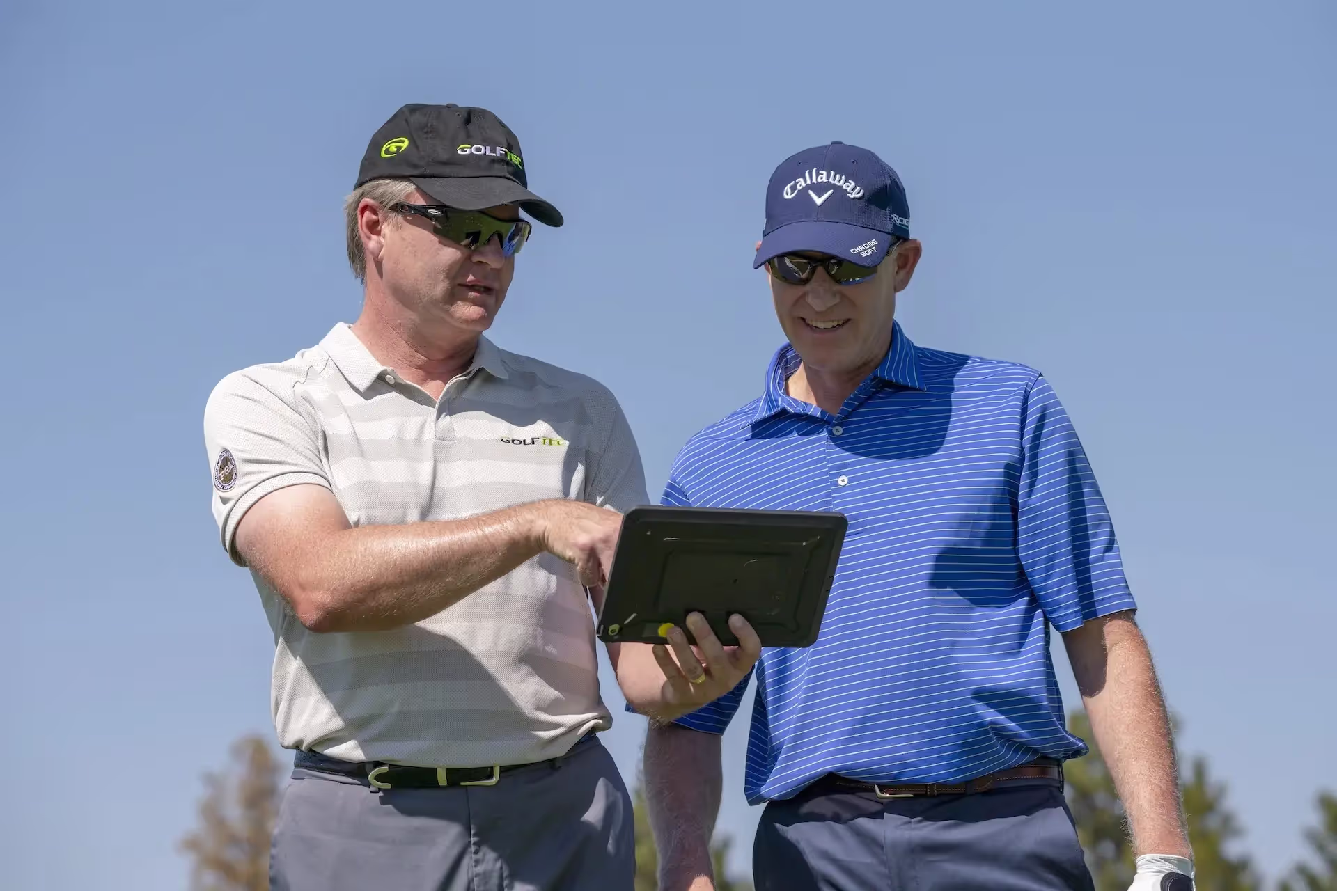 Student and GOLFTEC coach reviewing swings on an iPad during an outdoor lesson