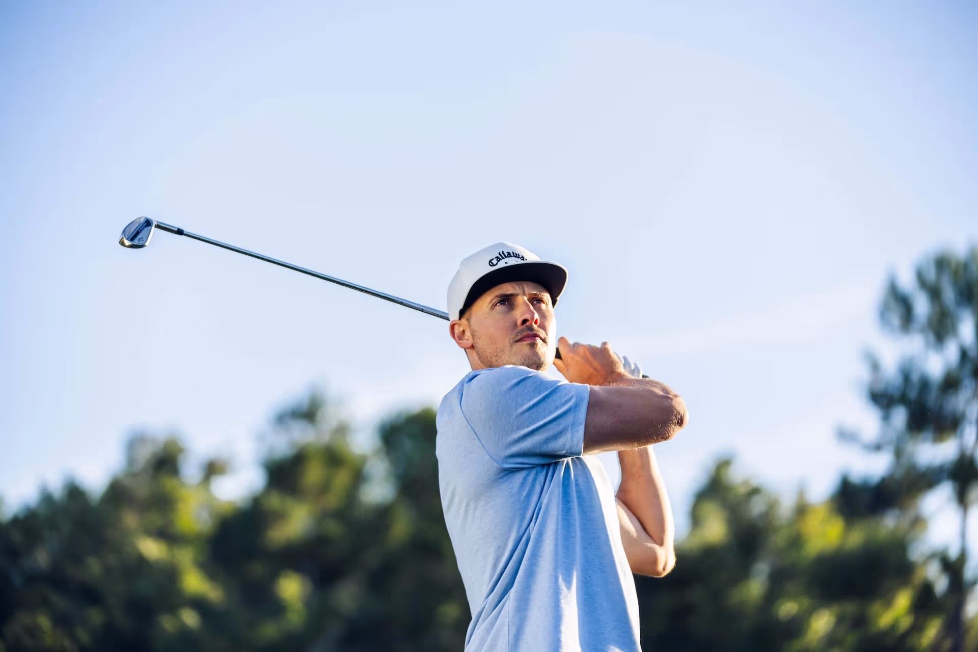 Golfer watching their shot in the backswing, holding a Callaway iron with trees in the background. 