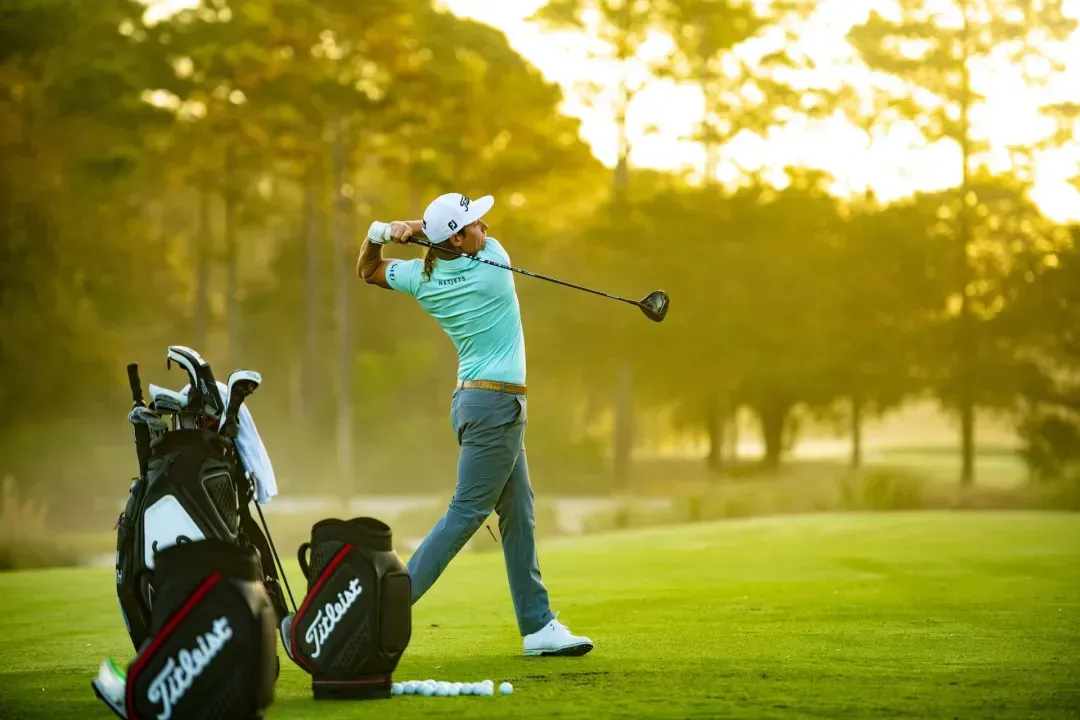 Golfer swinging a Titleist driver on the tee box next to their Titleist golf bag. 