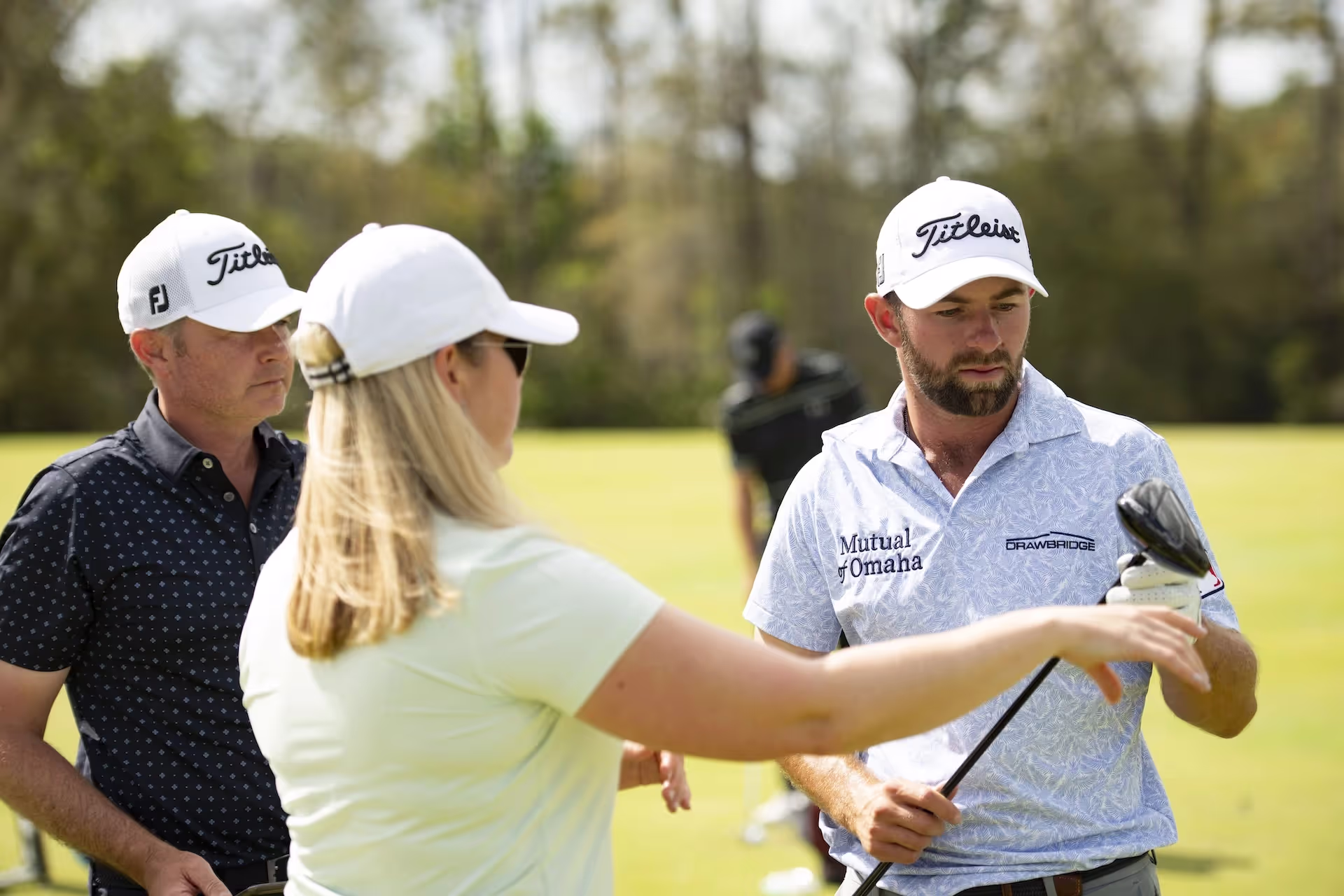 Golfer holding a Titleist club with three golfers in Titleist hats talking on the course. 