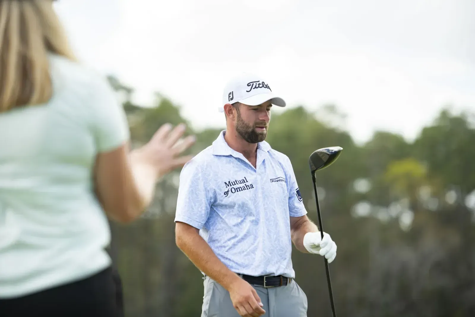 Golfer holding a Titleist club on the green with another golfer beside them.