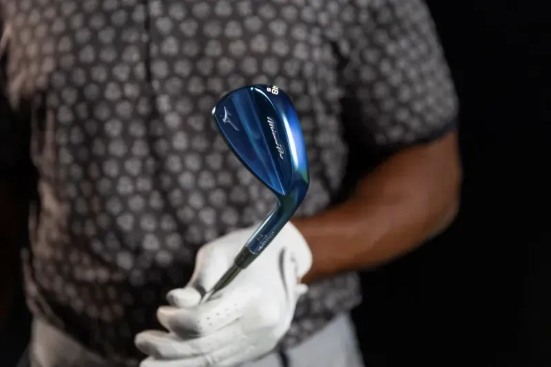 Golfer casually holding a blue Mizuno Pro T-1 wedge with his glove on, with his outfit in the background. 