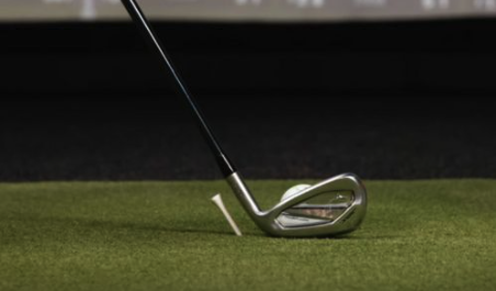 Iron aligned behind ball on turf beside tee for golf practice drill