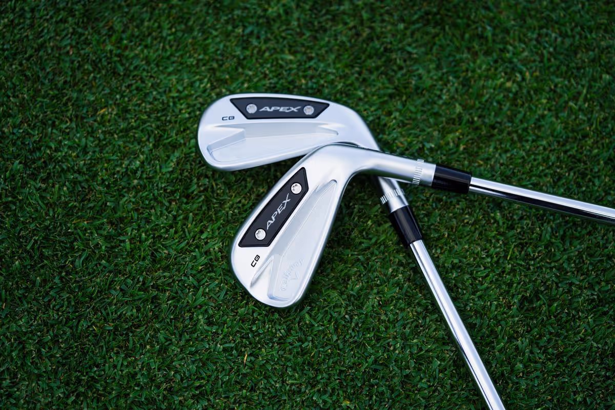 Two Callaway Apex CB irons lying on top of each other on the grass, showcasing their design. 