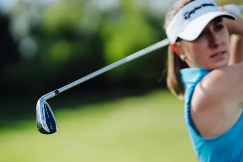 Close-up view of a female golfer in her backswing, holding a TaylorMade Qi iron and watching her shot.