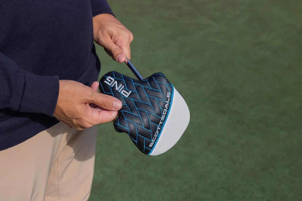 Man putting a putter head cover on his PING putter on golf course.