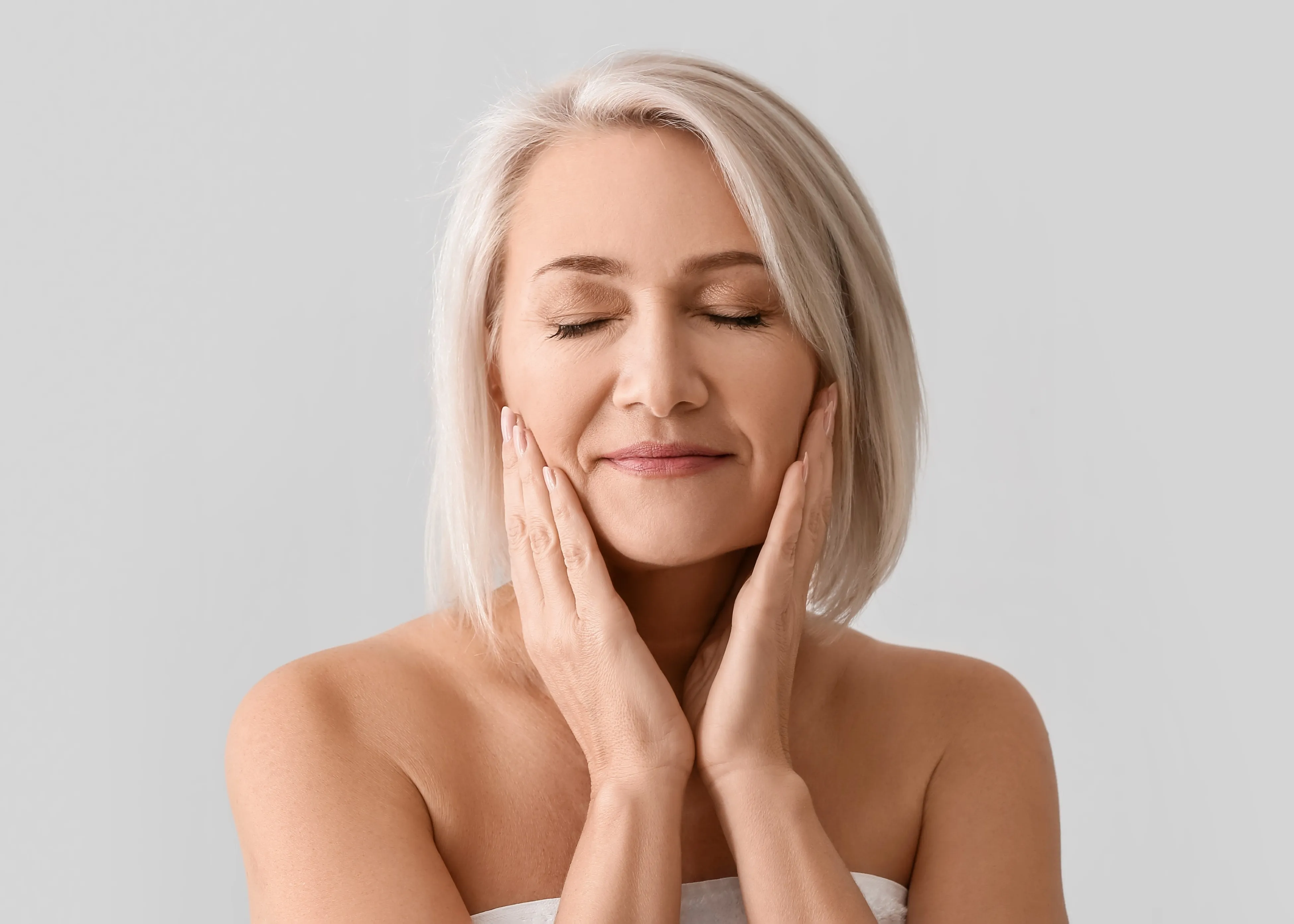 A woman with white hair is touching her face.
