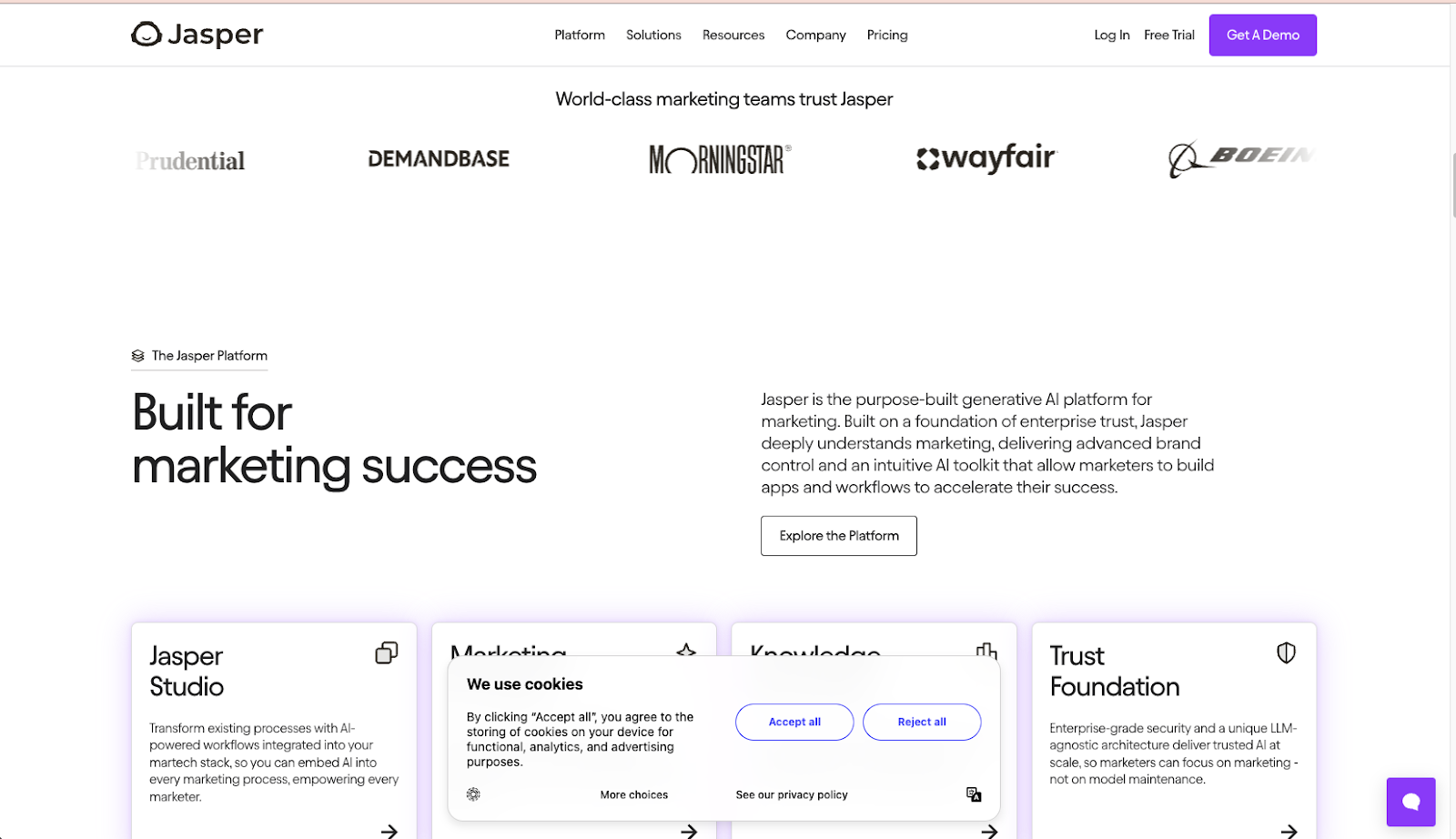 Screenshot of the Jasper website homepage showing their AI marketing platform. The header displays the Jasper logo and navigation menu. The main content reads "World-class marketing teams trust Jasper" with client logos including Prudential, Demandbase, Morningstar, Wayfair, and Boeing. A section titled "Built for marketing success" describes Jasper as a purpose-built generative AI platform for marketing with features for brand control and intuitive tools. The page also shows cards highlighting Jasper Studio, Marketing, Knowledge, and Trust Foundation features. A cookie consent dialog appears at the bottom of the screen.