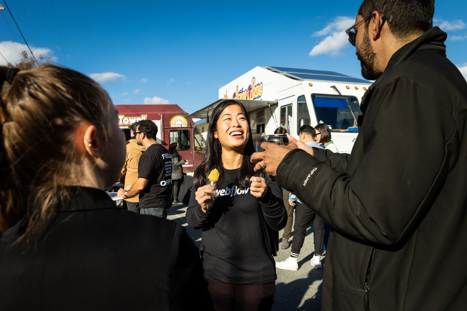 A woman smiles while holding a popsicle In front of two food trucks.