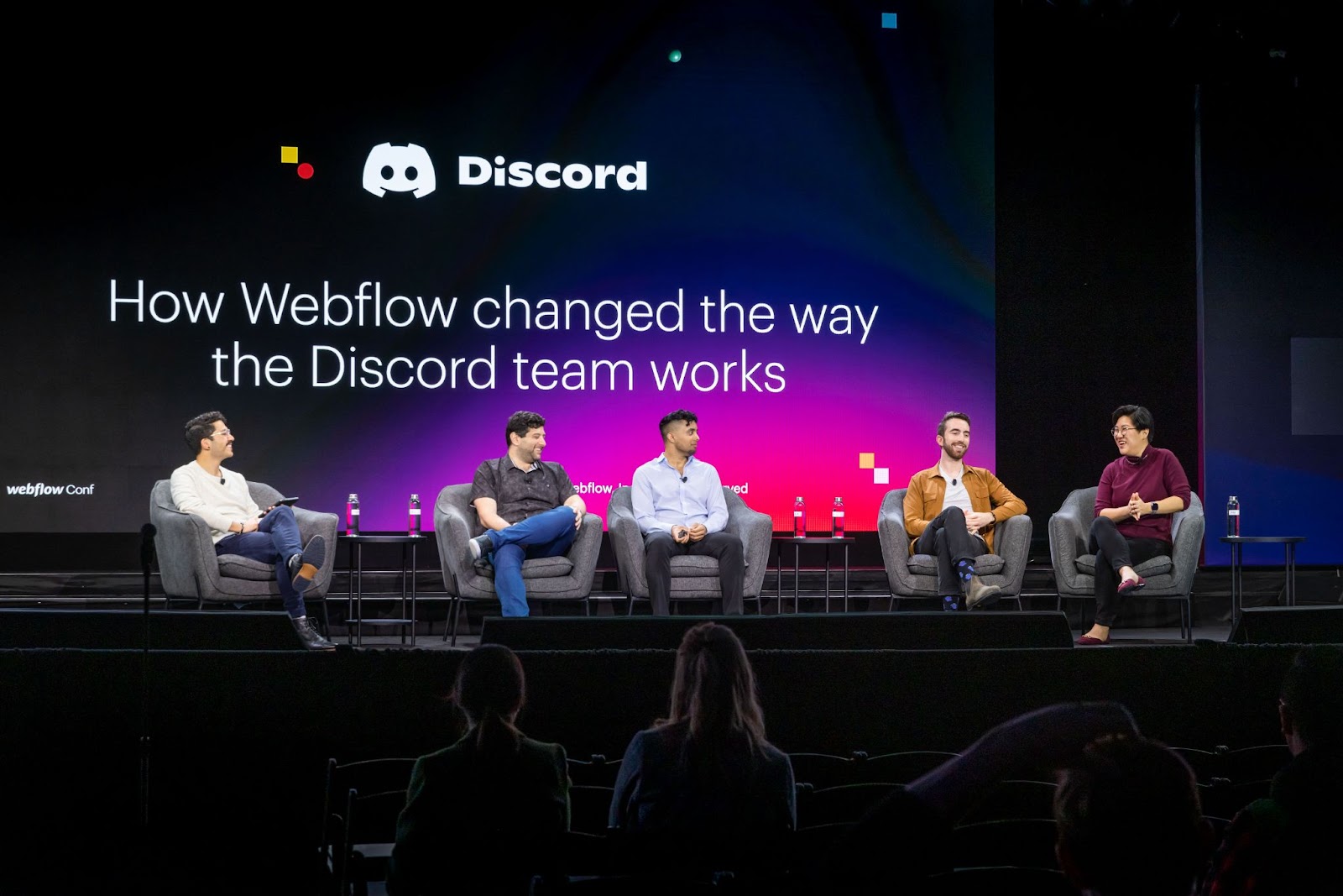 Photo of 4 people sitting in gray armchairs on stage in front of screen with headline "How Webflow changed the way the Discord team works.
