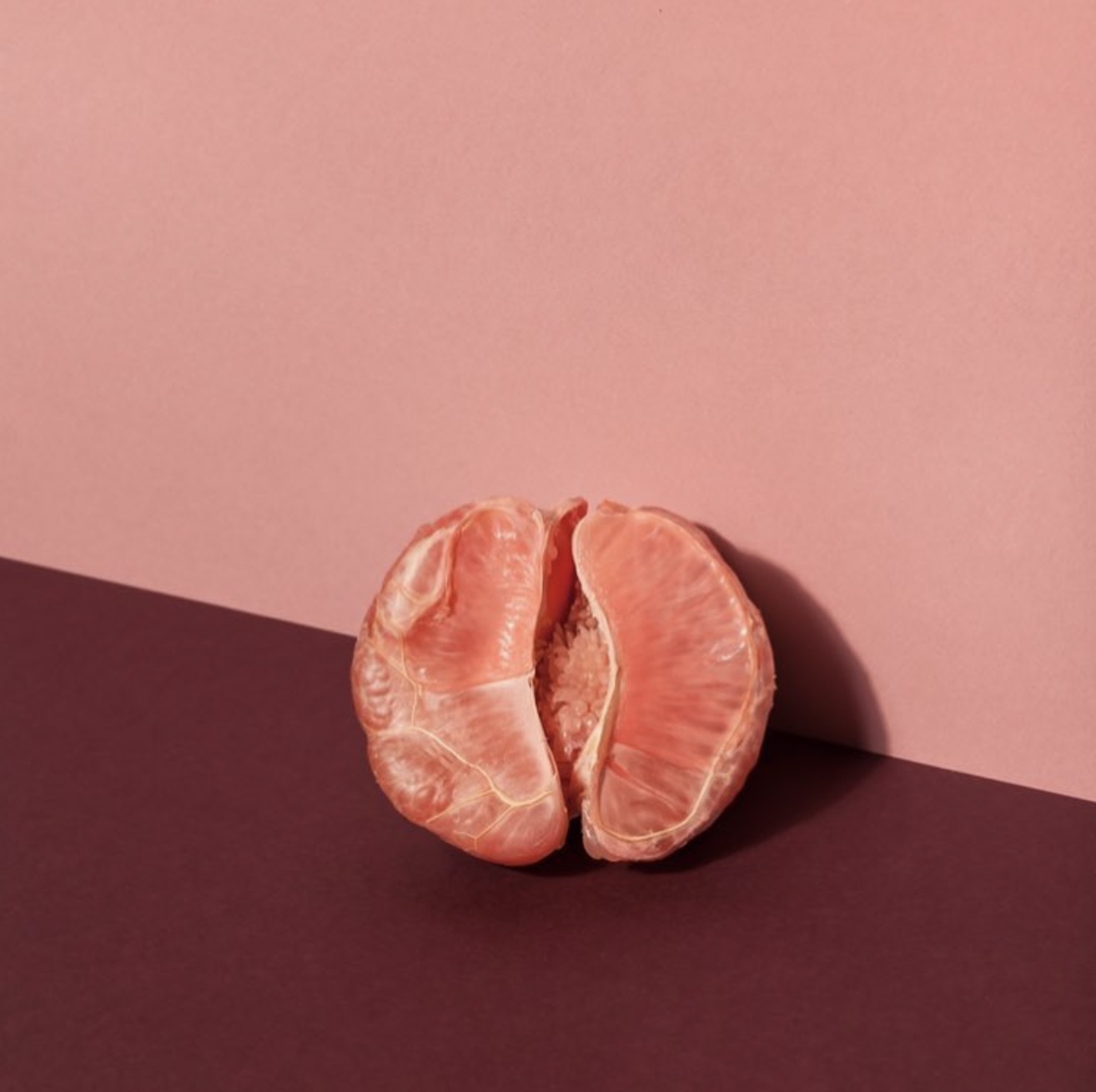 And image of half of a peeled grapefruit sitting on a two-tone mauve and burgundy background.
