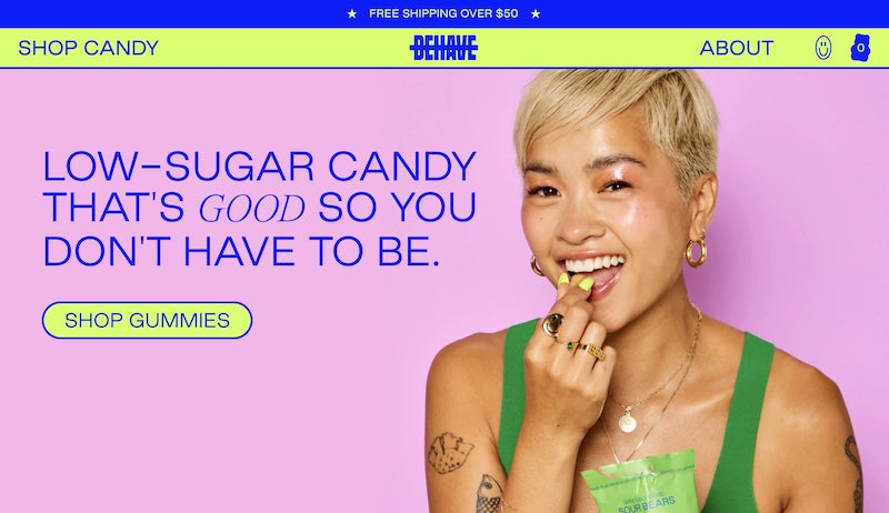 Pink landing page with large blue text reading “Low-sugar candy that’s good so you don’t have to be” on the left and an image of a woman eating a piece of candy on the right.
