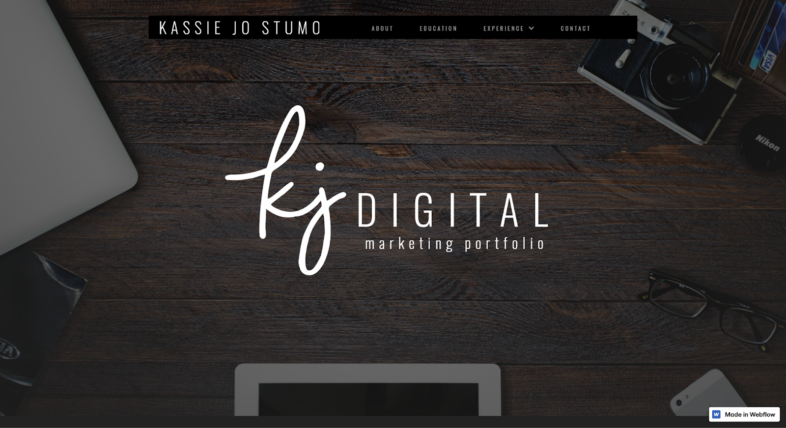 Kassie Jo’s portfolio has the text “KJ Digital” in the middle, with a wooden table and other tech items as a background.