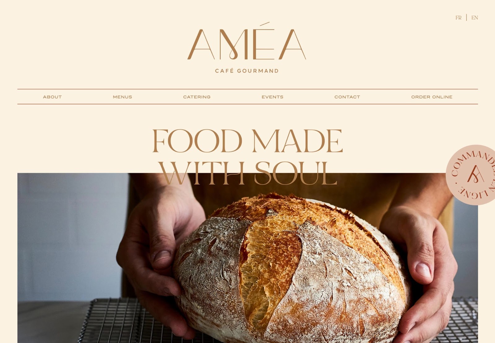 Améa homepage. Beige background. Golden-brown text "FOOD MADE WITH SOUL" over a large photo of hands holding a round loaf of crusty bread.