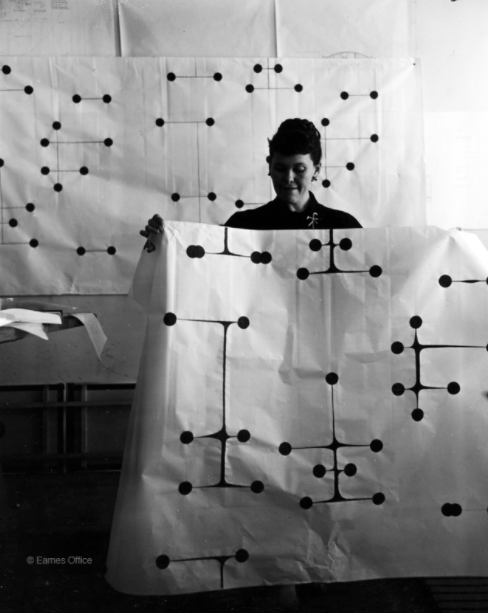 Ray Eames holding up a pattern in a studio space.