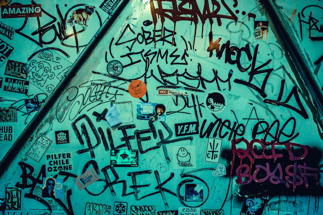A photo of a turquoise wall covered in different graffiti tags and stickers.