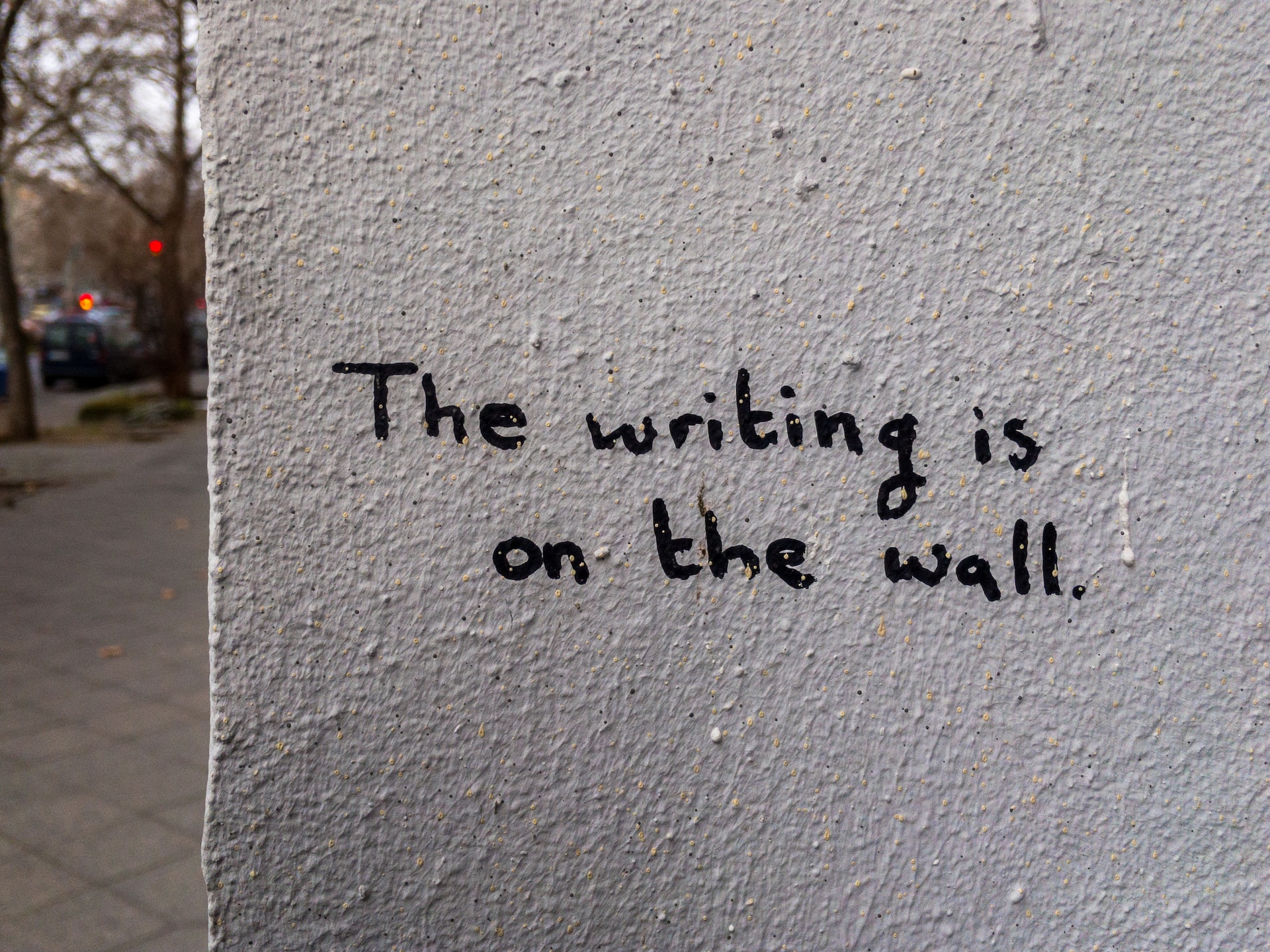 The words “The writing is on the wall” on a wall in regular handwriting.