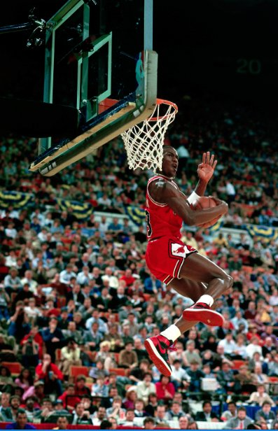 Photo of Michael Jordan mid-air before dunking in front of a packed crowd in the the 1995 Slam Dunk contest as he wears his red Chicago Bulls uniform and black and red Air Jordans