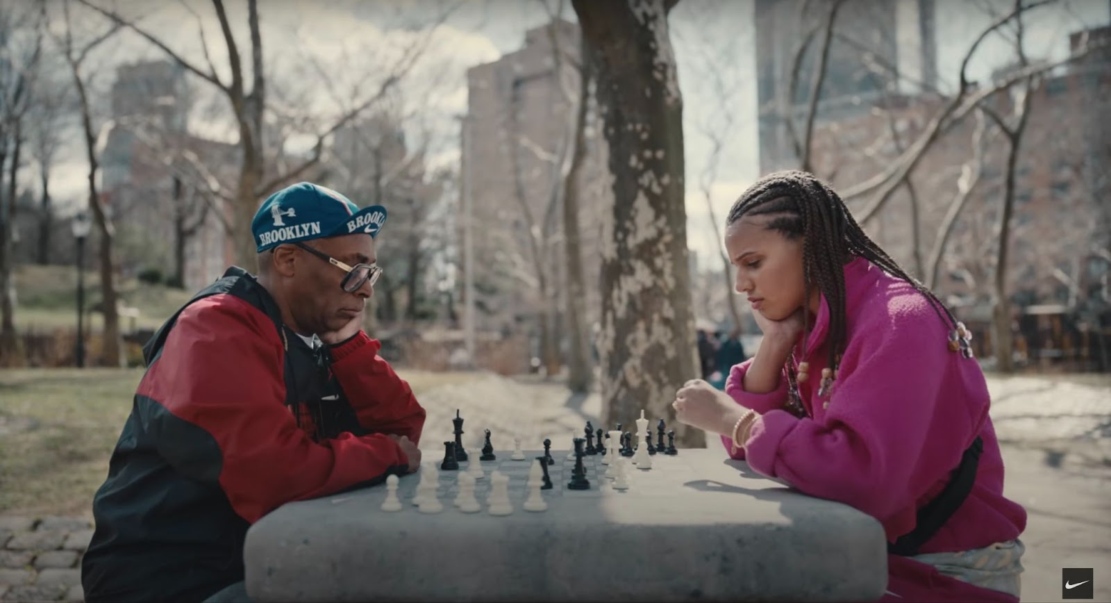 Spike Lee and a woman play chess in a New York City park.
