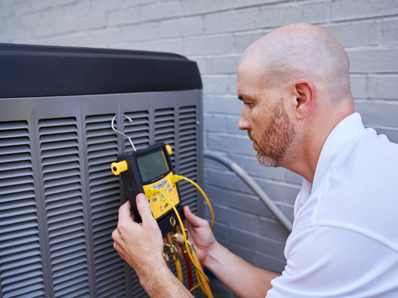 Technician checks outdoor AC unit pressure.