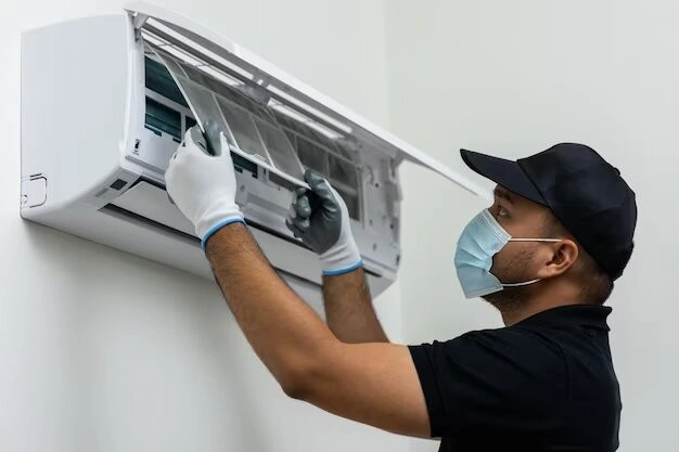 Technician replacing mini-split AC filter, wearing mask.
