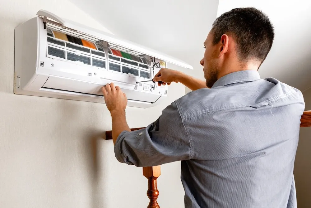 Man repairs AC unit on wall.