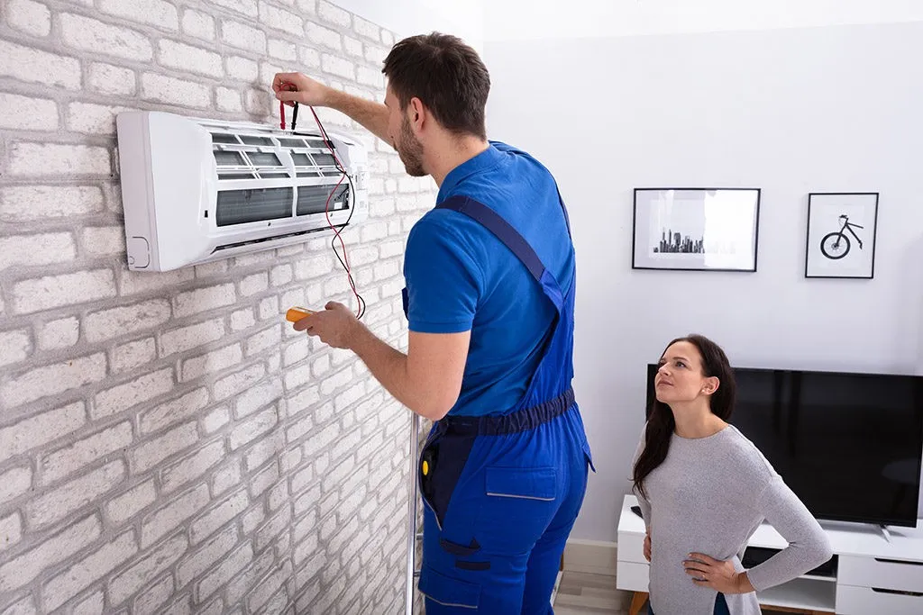 Technician diagnoses wall AC while woman watches.