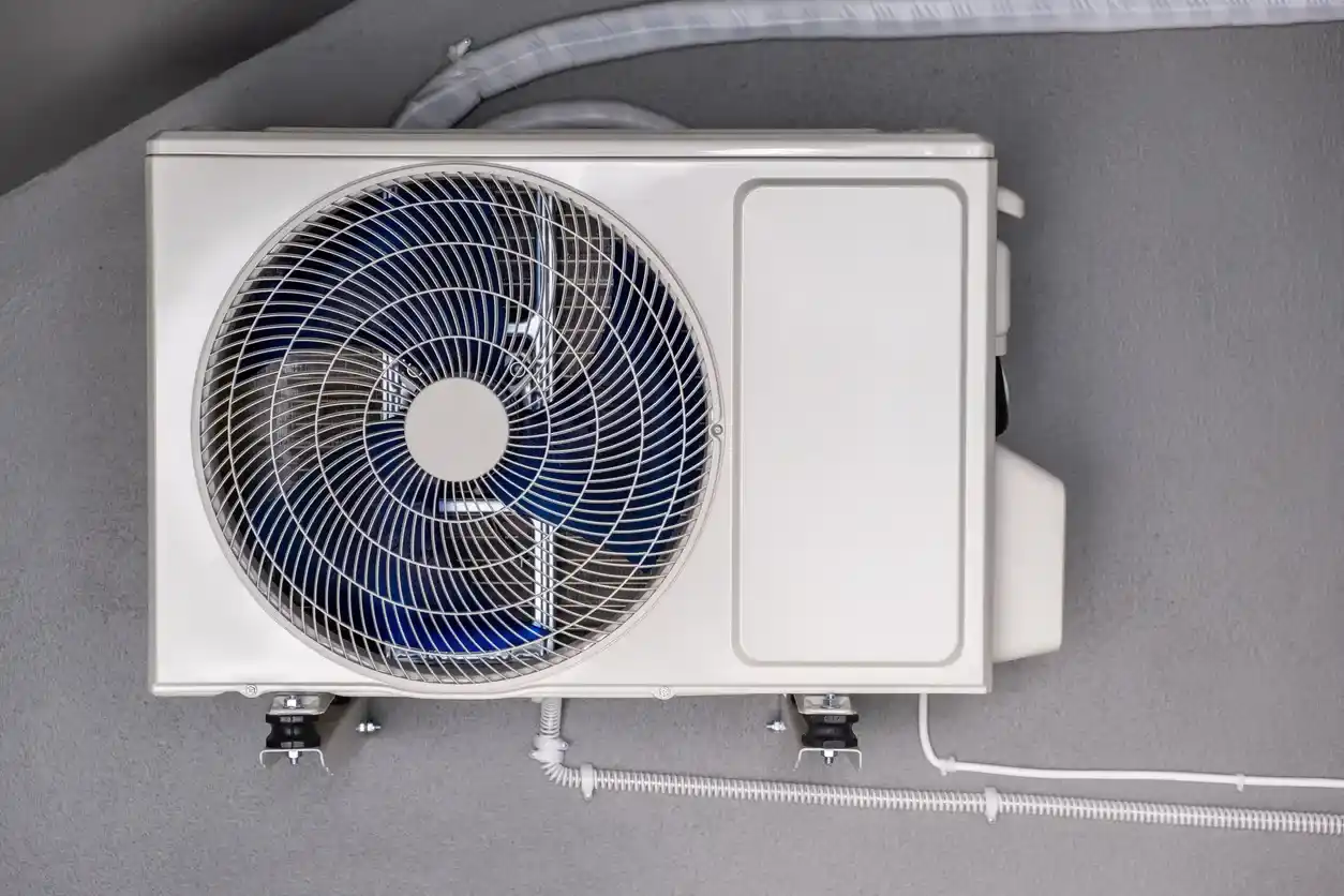 A close-up of a large outdoor mini-split unit with its fan spinning against a gray wall.