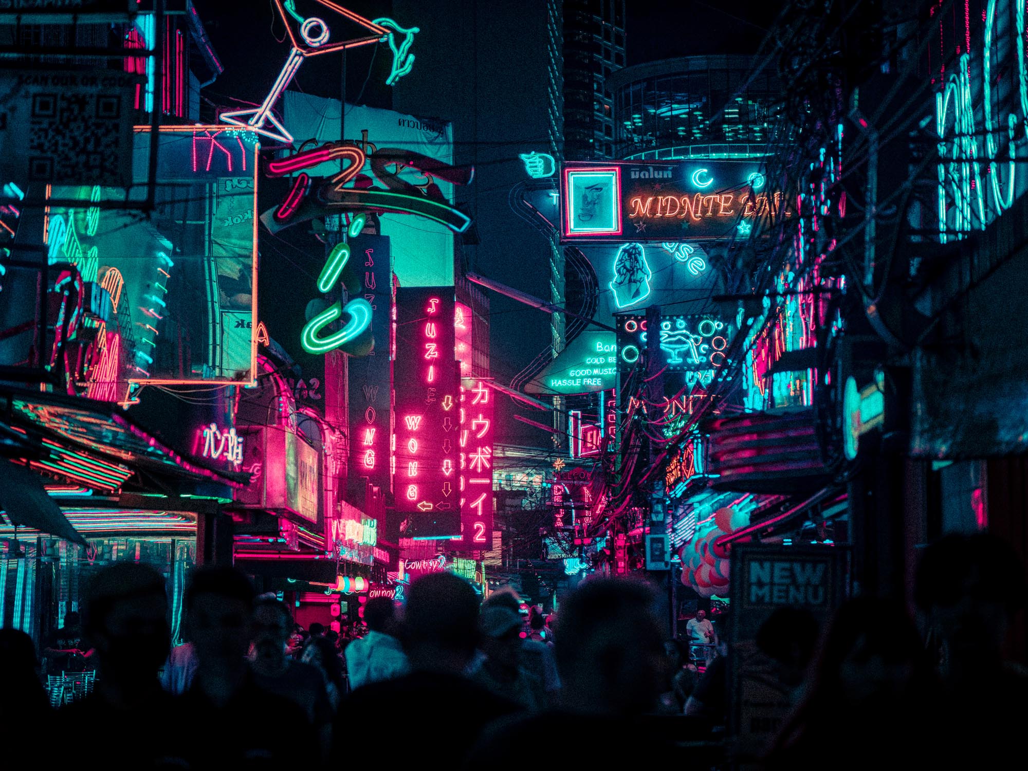 Crowded urban street at night illuminated by neon signs in blue, pink, and red hues.