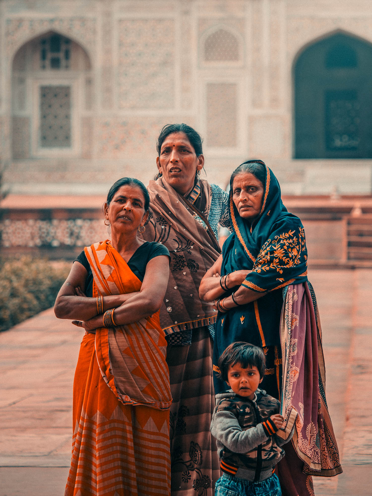 Three Indian women in traditional sarees standing with a young boy in front of an ornately decorated historical building.