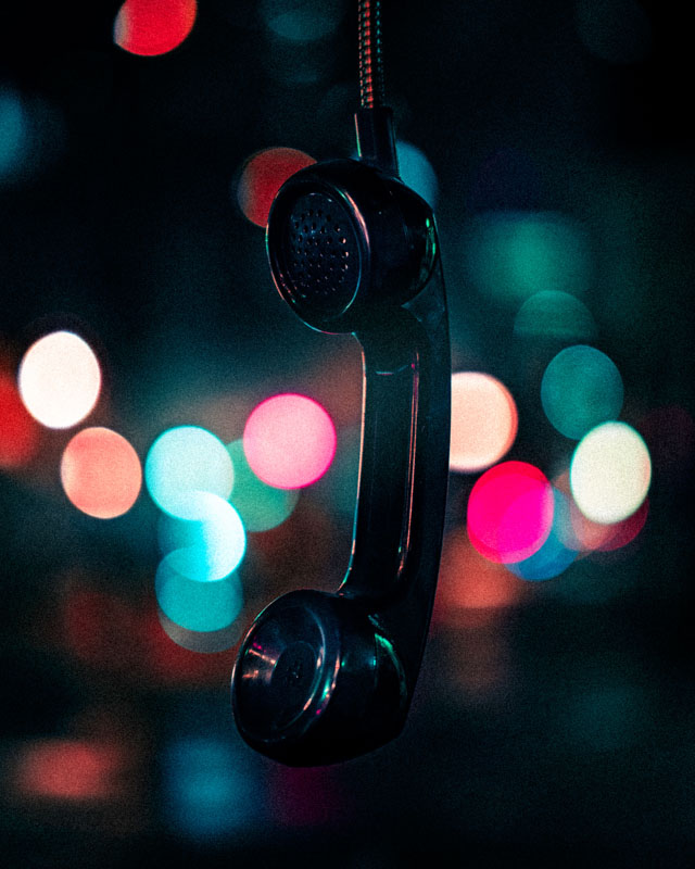 Black vintage telephone handset hanging against a blurred background with colorful bokeh lights.