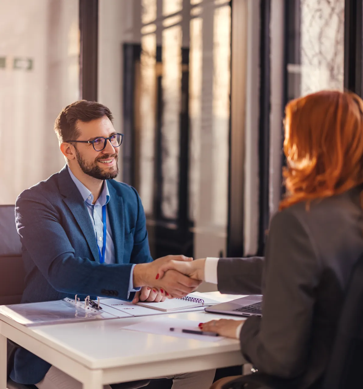 2 business people shaking hands while sitting at a desk
