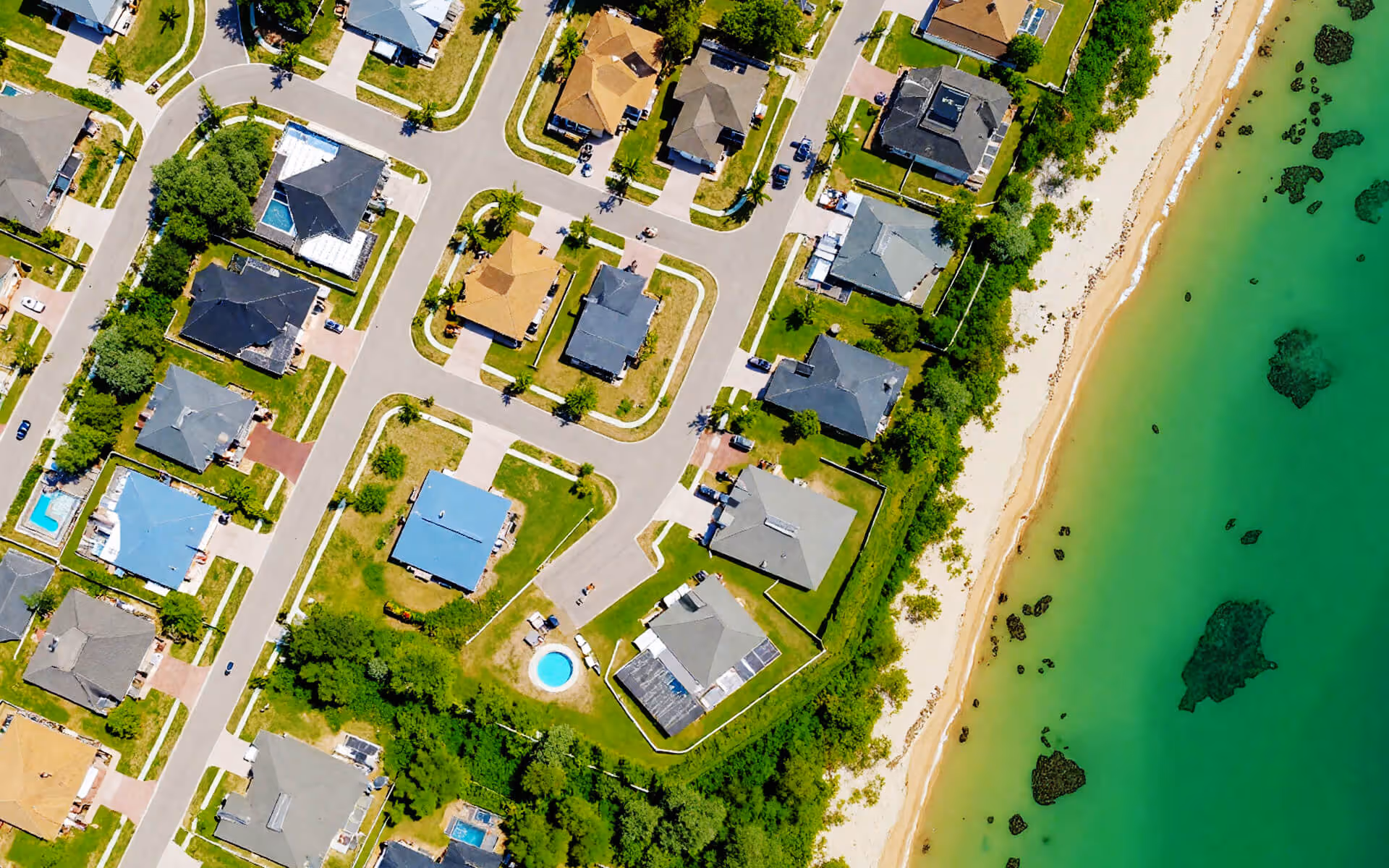 A vibrant aerial view of Clearwater, Forida. It showcases a well-planned residential neighborhood adjacent to a serene beach, where pristine sandy shores meet turquoise waters. 