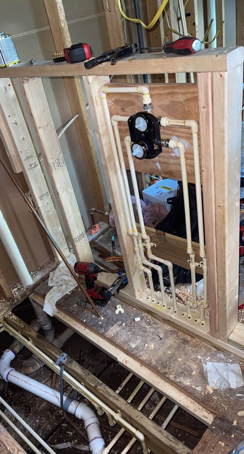 Construction site showing framed wooden wall with installed PVC plumbing pipes and tools on a workbench in a basement or utility room.