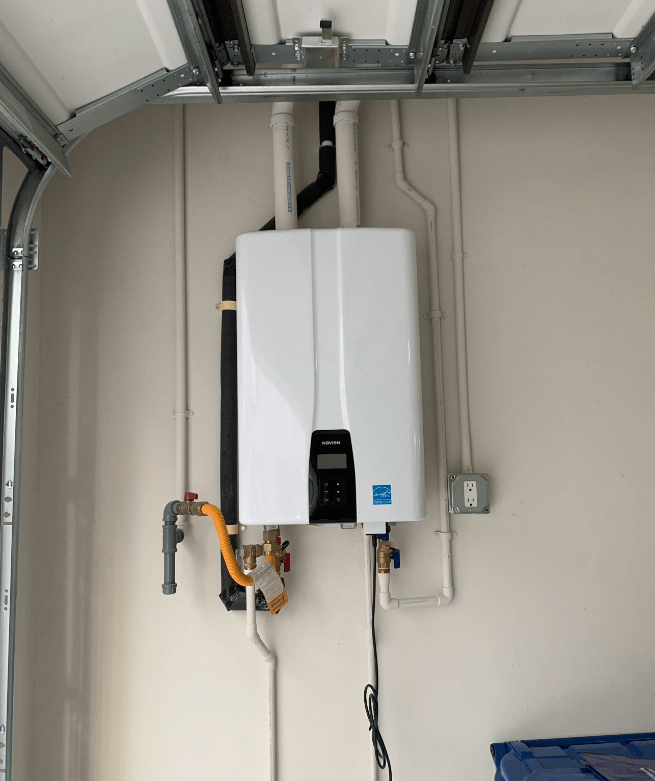 Wall-mounted Navien tankless water heater with connected pipes and a power outlet on the right.