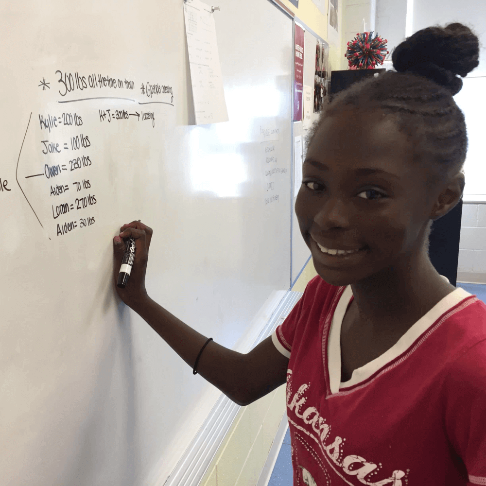 Student writing math on a whiteboard with a big smile