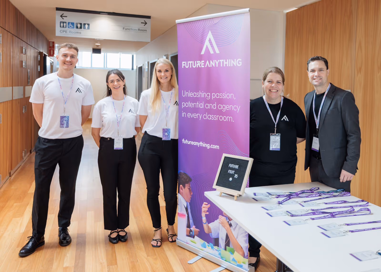 Five people standing indoors next to a purple banner reading 'Future Anything' with a table displaying event badges.