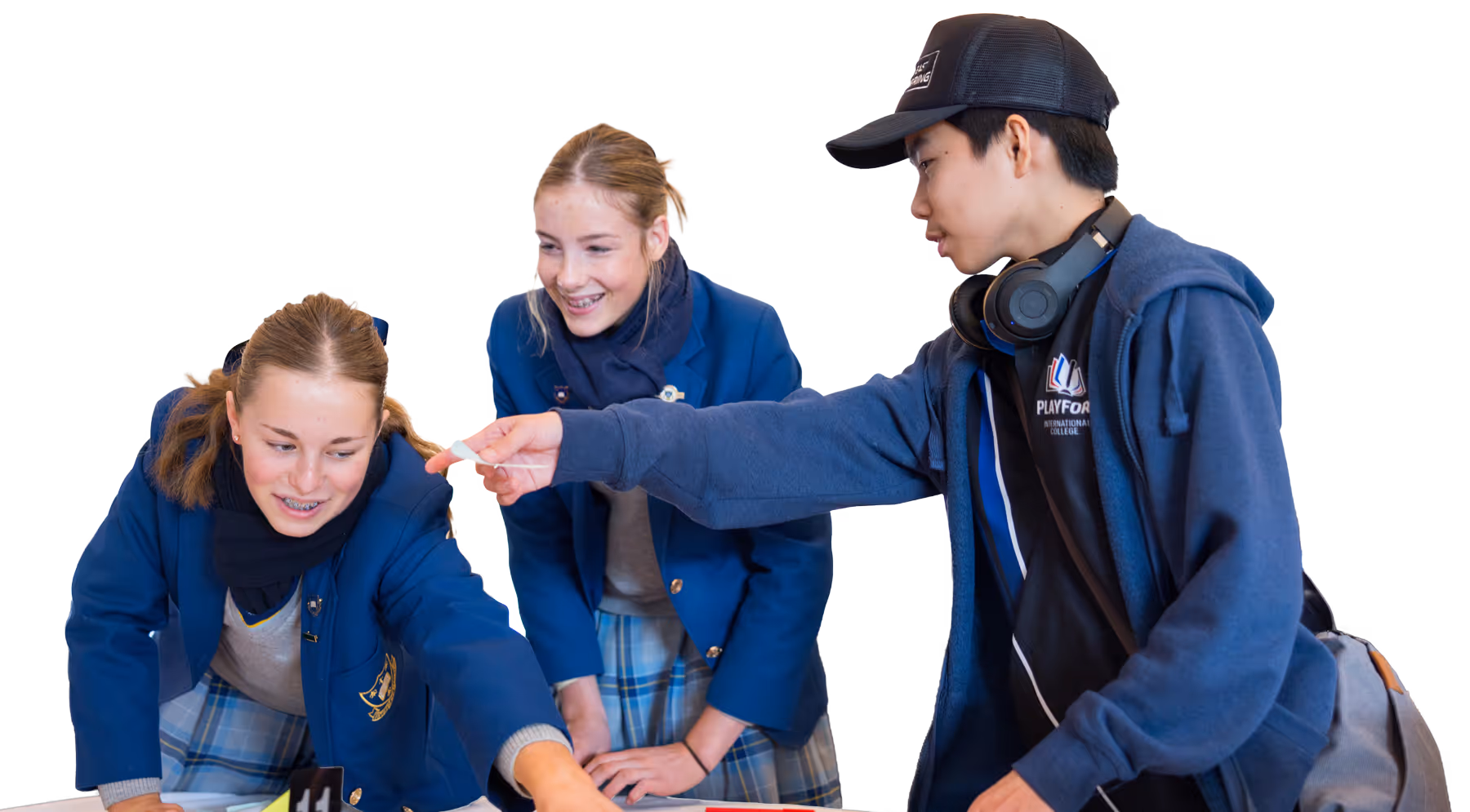Three students in school uniforms, two girls and one boy, interacting and smiling while looking at something on a table.